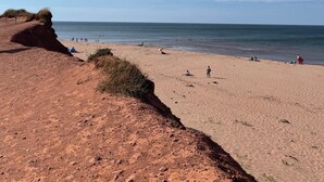 A beach with a clear sky, sandy shore, and rocky cliffs. - Ocean Edge Beach House (Malpeque)