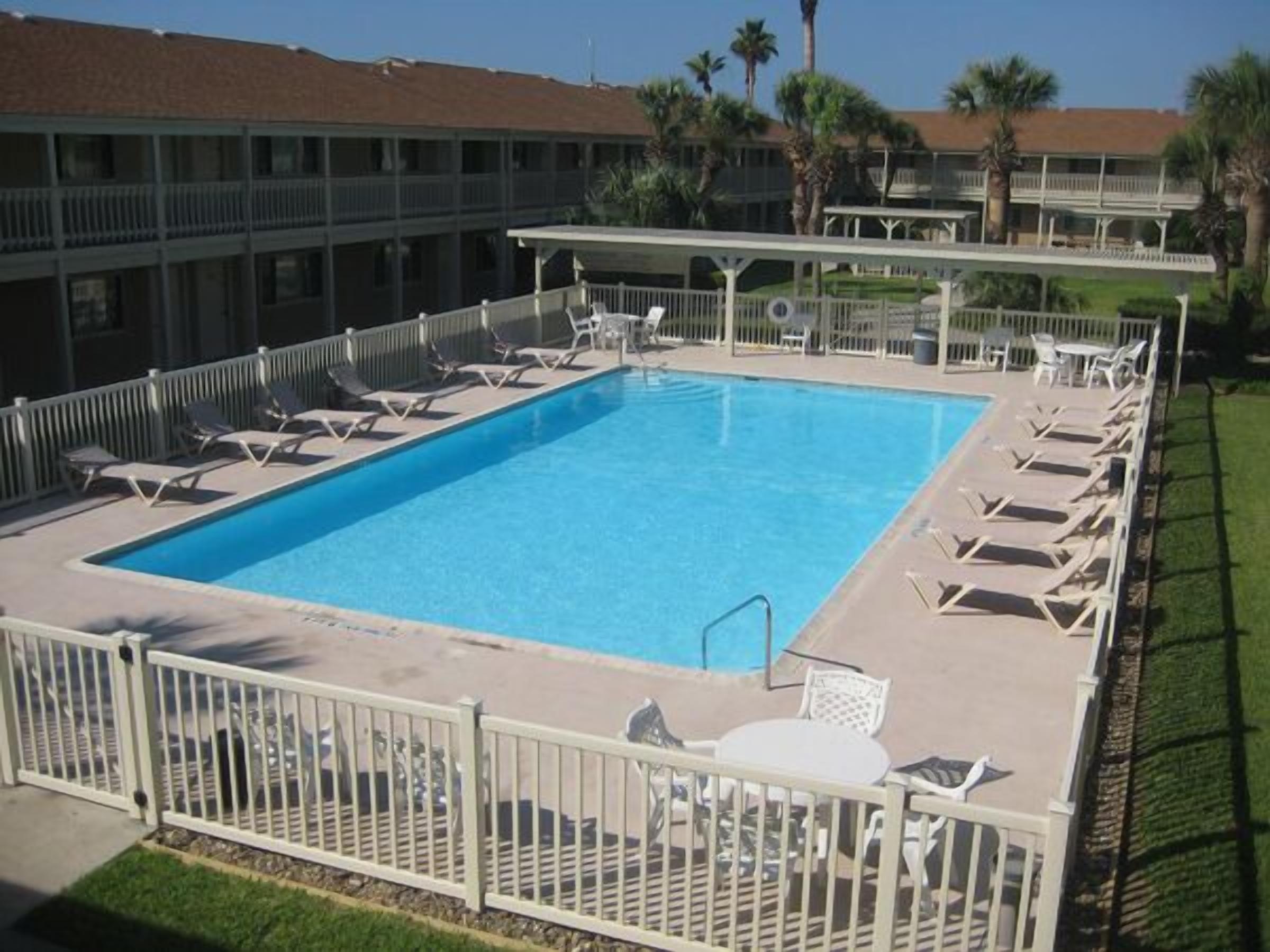 A rectangular pool with white lounge chairs and a white fence surrounding it.
