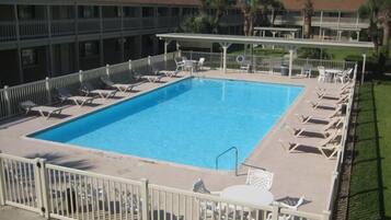 A rectangular pool with white lounge chairs and a white fence surrounding it.