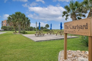 Une enseigne indiquant « The Courtyard Port Aransas, TX », avec des tables de pique-nique et des parasols dans un espace verdoyant.