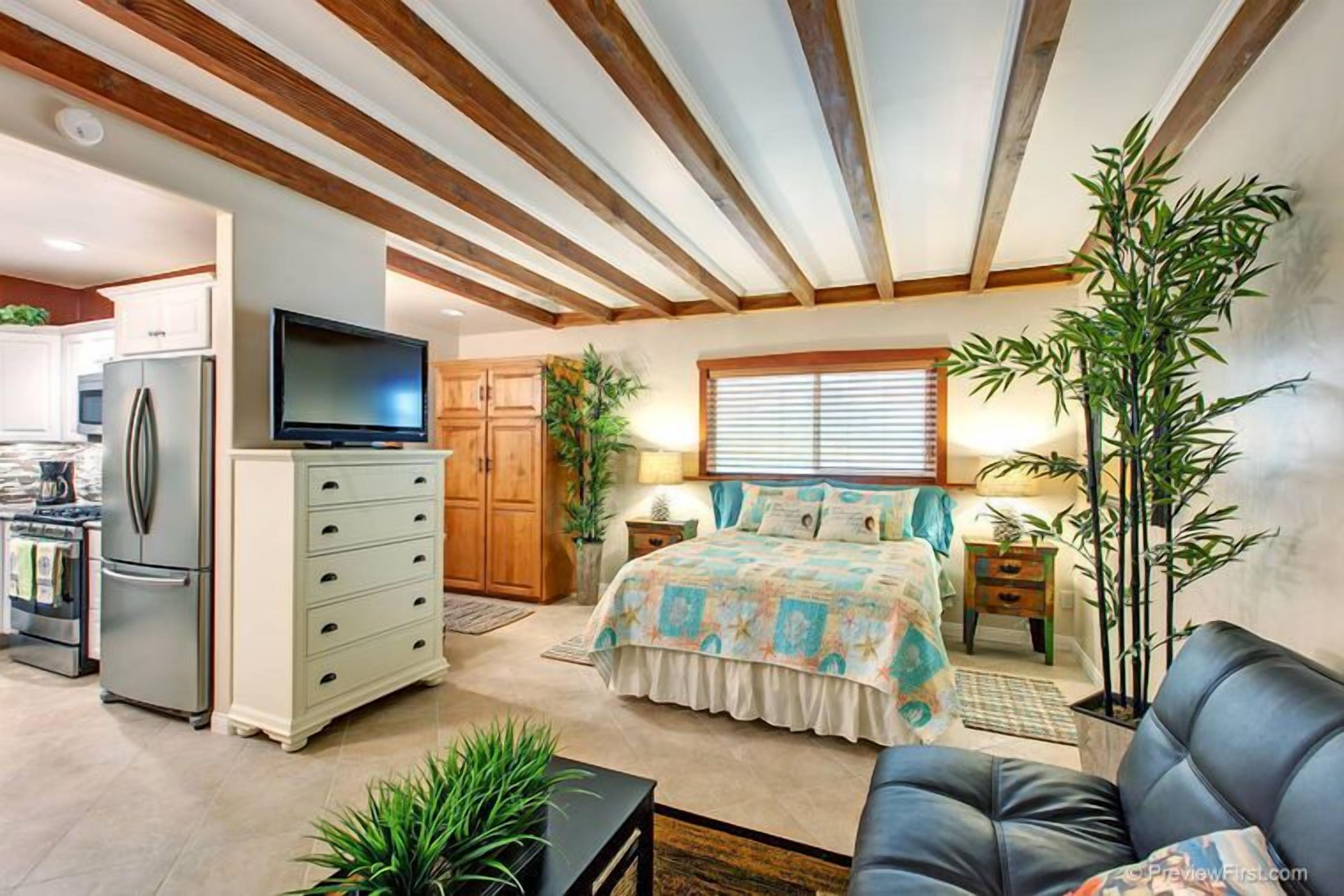 A bedroom with a bed, a television, a dresser, and a window with blinds.