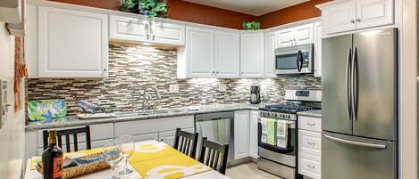 A modern kitchen with white cabinets, a stainless steel refrigerator, a microwave, and a gas stove.