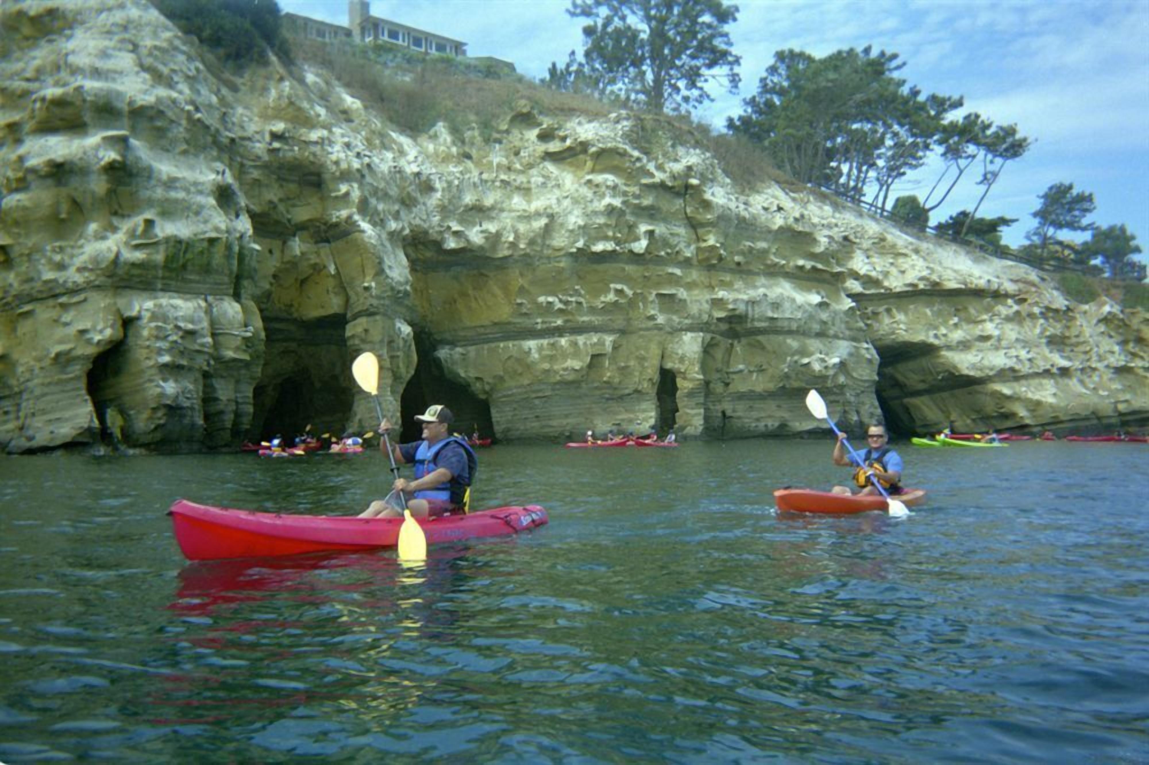 Des kayakistes sur une étendue d’eau calme, près de falaises rocheuses.