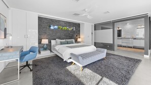 Un dormitorio moderno con una cama grande, un escritorio y una silla. Se ve una ventana con vistas a árboles.