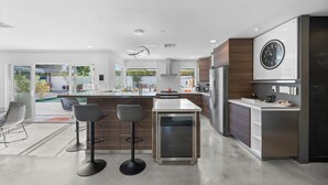 Una cocina moderna con una isla central, taburetes de bar, horno integrado y un reloj de pared grande.