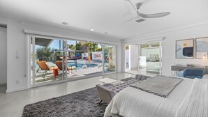 Un dormitorio moderno con una cama grande, un ventilador de techo y vistas a una piscina exterior.