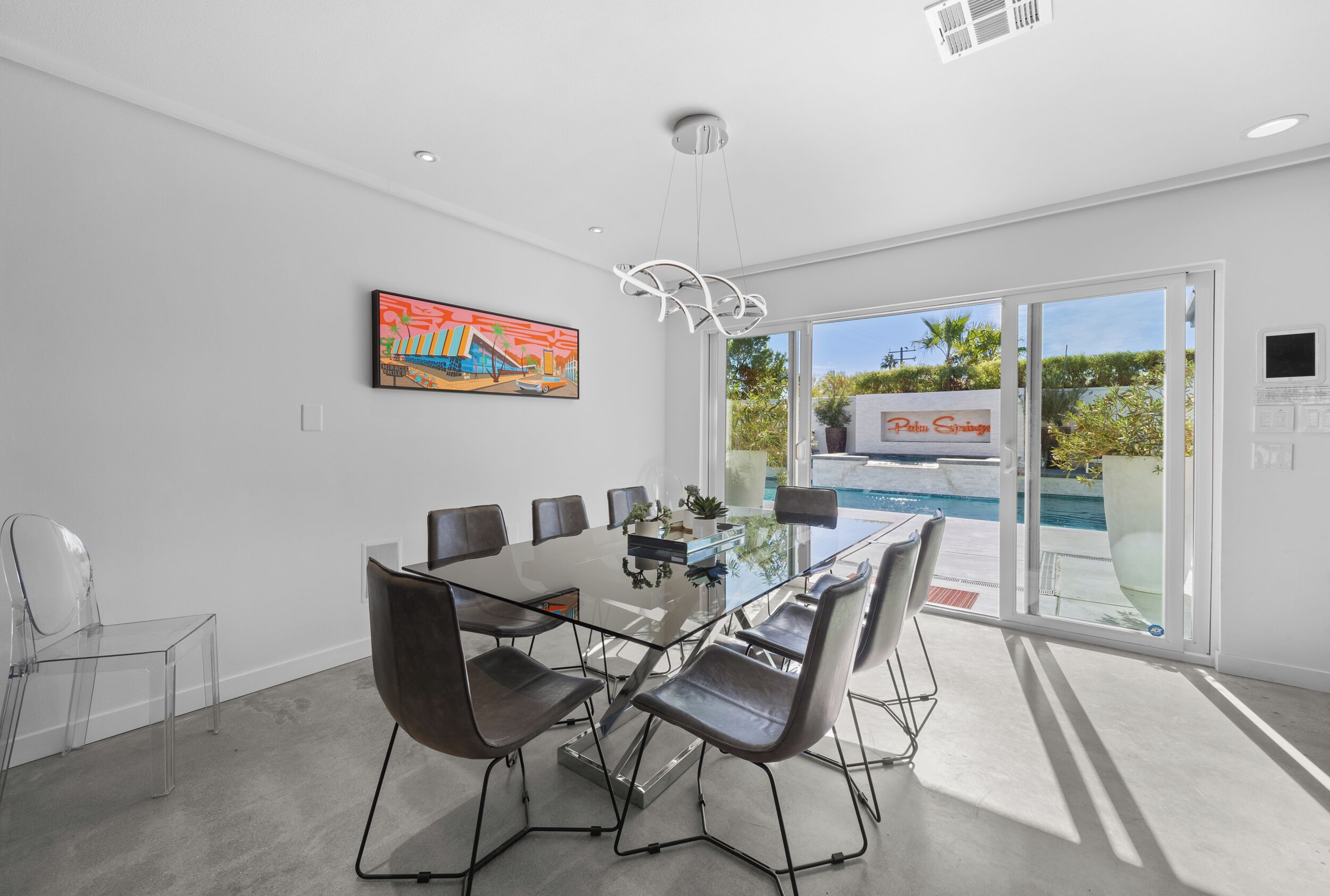 A modern meeting room with a glass table, six chairs, a painting on the wall, and a view of a pool outside.