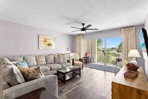 A living room with a sofa, armchairs, a coffee table, a ceiling fan, and a view of the outdoors through a sliding glass door.