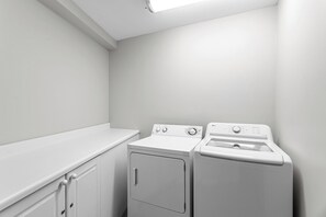 A laundry room with a washing machine and dryer, white walls, and a countertop. - Amalfi Coast 213B - Community Pool, Fitness Facility, Gulf Views, Miramar Beach! (Miramar Beach)