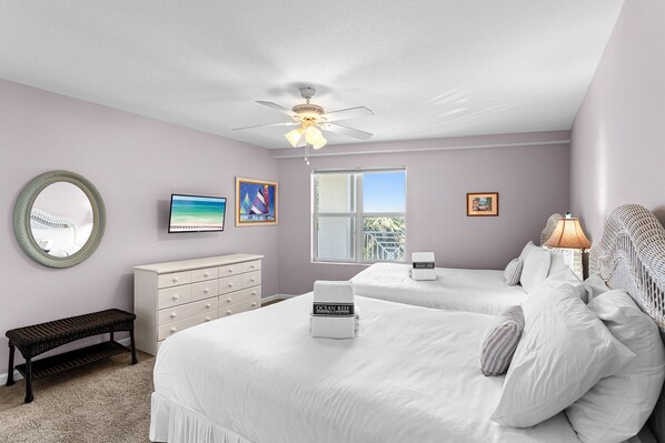 A bedroom with two beds, a ceiling fan, a TV, and a window with a view. - Amalfi Coast 213B - Community Pool, Fitness Facility, Gulf Views, Miramar Beach! (Miramar Beach)
