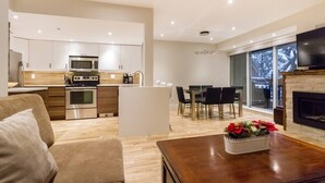 A modern living space with a kitchen, dining area, and a fireplace. - Private Hot Tub & AC | Pool | Free Parking | Steps to Village, Lifts & Bike Park (Whistler)
