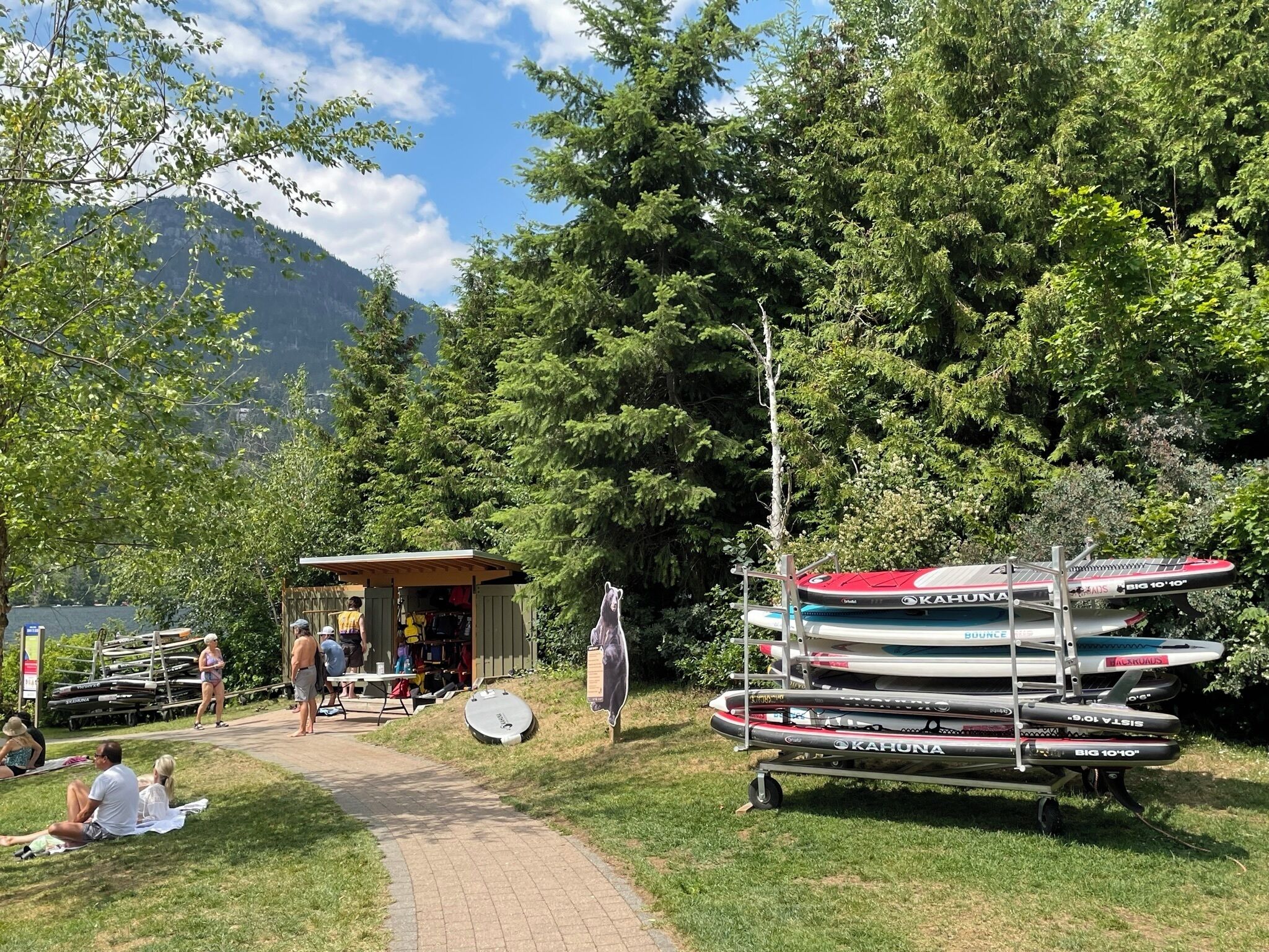 A lakeside setting with a small wooden structure, kayaks, and a paddleboard.