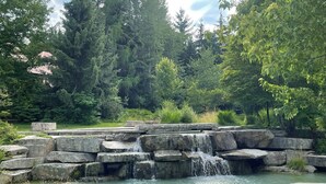 A natural landscape with a small waterfall, surrounded by dense trees and a clear sky. - Private Hot Tub & AC | Pool | Free Parking | Steps to Village, Lifts & Bike Park (Whistler)