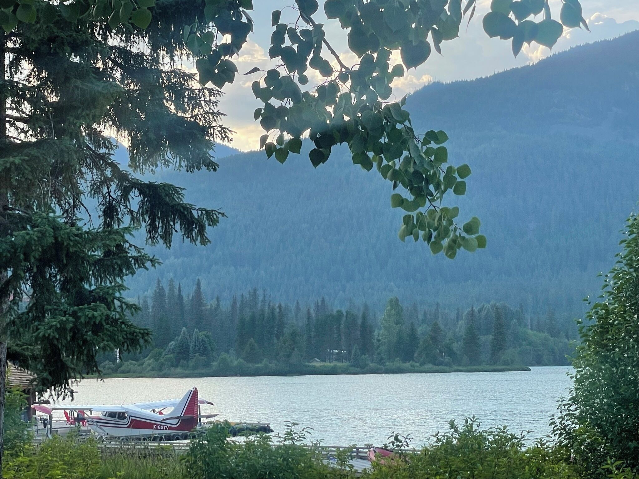 A lake with a small airplane on the shore, surrounded by trees and mountains.
