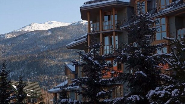 A multi-story lodge with a mountain backdrop, featuring a prominent balcony and a snow-covered roof. - Private Hot Tub & AC | Pool | Free Parking | Steps to Village, Lifts & Bike Park (Whistler)