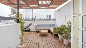 A rooftop patio with a wooden deck, a gray sofa, a small table, and potted plants. - Penthouse in Centro Historico with 2 Bedroom/2 Bathroom & Private Terrace (Centro)
