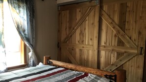 A bedroom with a wooden wardrobe, a bed with a striped bedspread, and a window with curtains. - Charlie’s house on the lake (Nikiski)