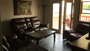 A living room with a brown leather sofa, a wooden coffee table, and a painting on the wall. - Charlie’s house on the lake (Nikiski)
