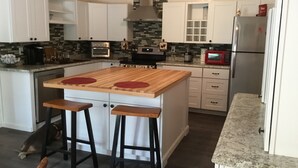 A modern kitchen with white cabinets, a wooden island with stools, a built-in oven, and a refrigerator. - Charlie’s house on the lake (Nikiski)
