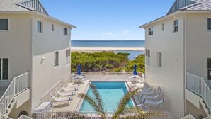 Ein Poolbereich mit Liegestühlen und Sonnenschirmen mit Blick auf einen Strand und das Meer.
