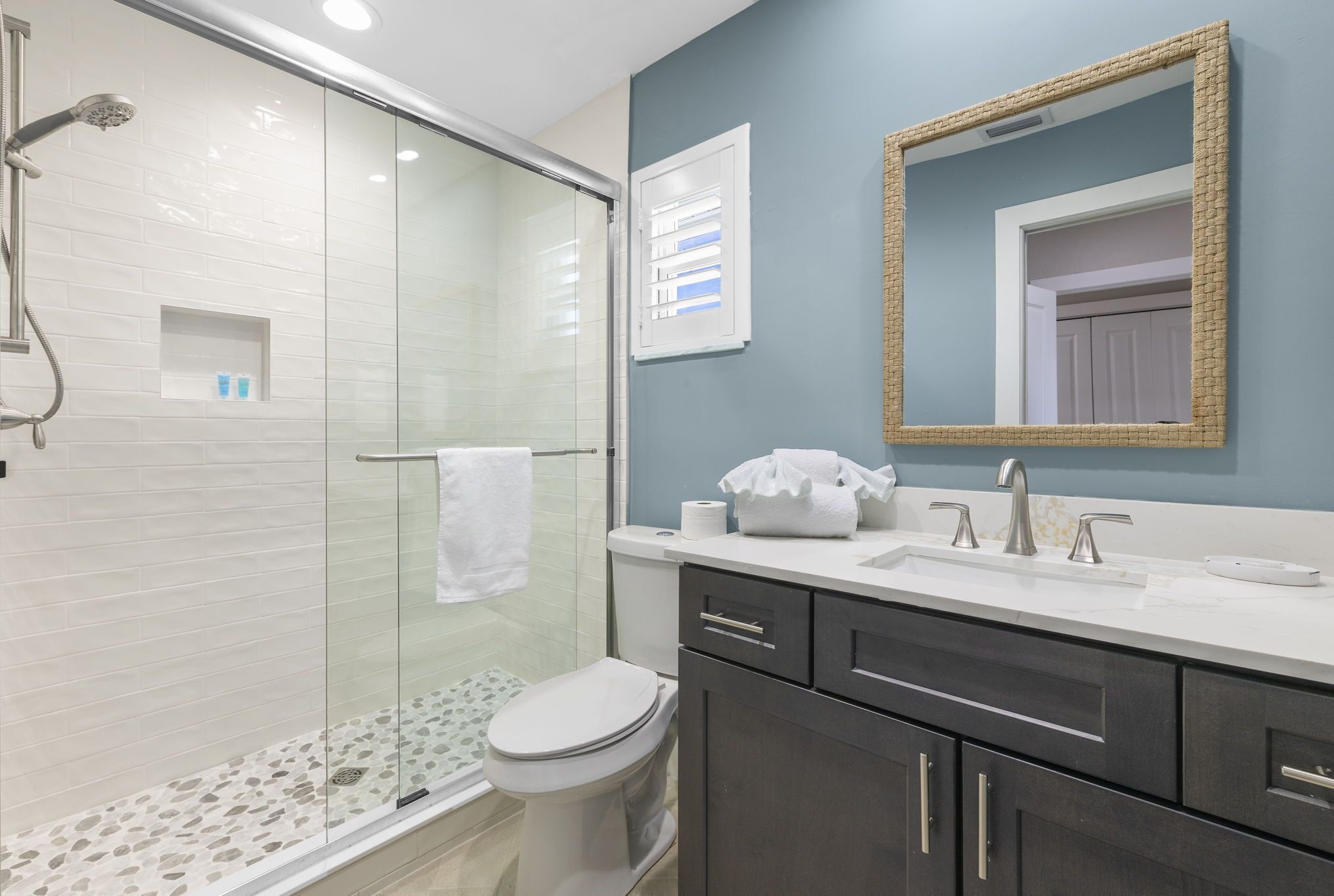 A modern bathroom with a glass-enclosed shower, a toilet, and a sink with a mirror above.