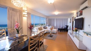 A modern living room with a glass dining table, a sofa set, and a TV mounted on the wall. - Unobstructed Ocean View Suite. Don't miss out on the last-minute special rate! (Honolulu)