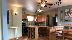 Una cocina moderna con armarios de madera, una isla central con taburetes, electrodomésticos de acero inoxidable y un ventilador de techo.