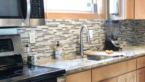 Una cocina moderna con electrodomésticos de acero inoxidable, salpicadero de azulejos, armarios de madera y una ventana con persianas.