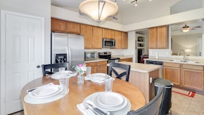 A modern kitchen with wooden cabinets, stainless steel appliances, and a dining area set for four. - 3BR w pool, putting green, fire pit (Gilbert)
