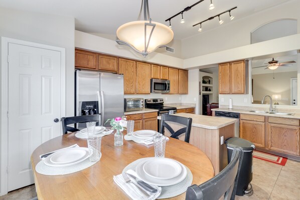A modern kitchen with wooden cabinets, stainless steel appliances, and a dining area set for four.