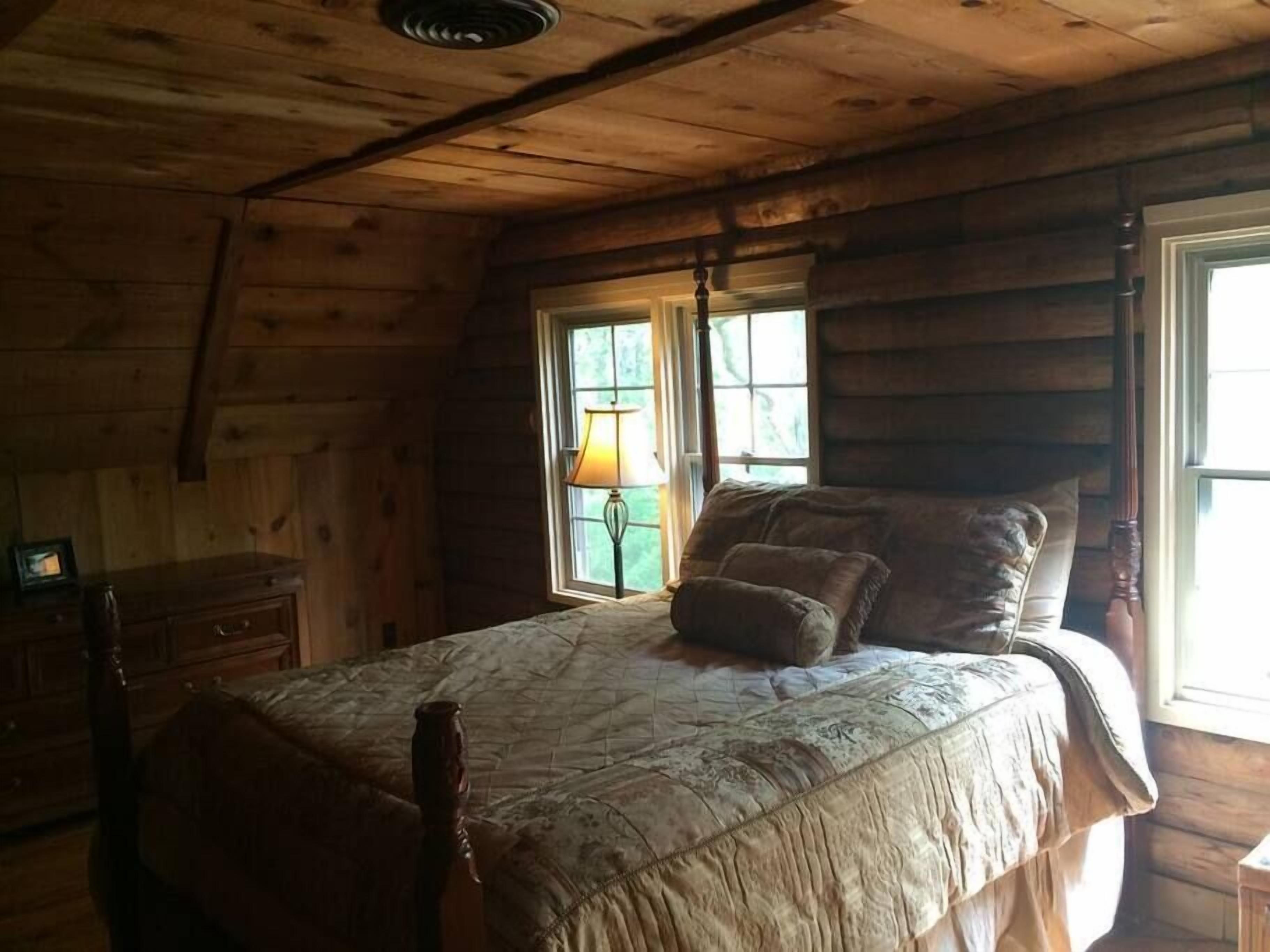 A wooden cabin bedroom with a bed, a nightstand, a lamp, and a window.