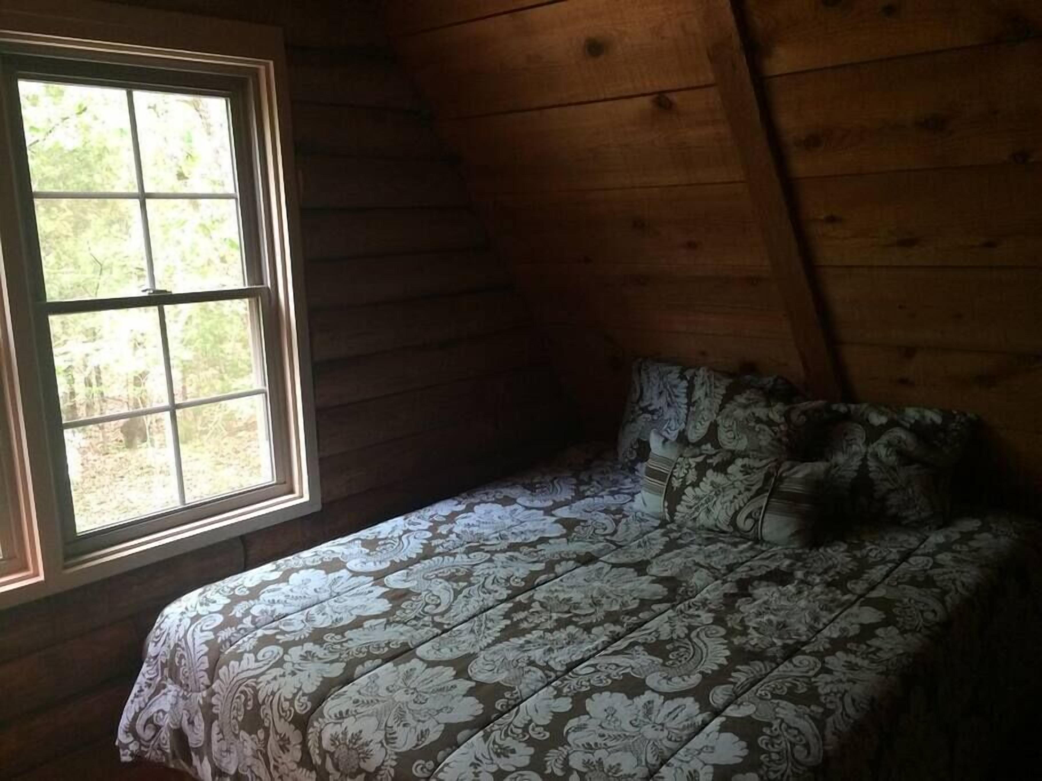 A bedroom with a wooden sloped ceiling, a window, and a bed with patterned bedding.
