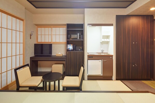 Un espacio habitable compacto con kitchenette, televisor, zona de estar y una puerta corredera tradicional.