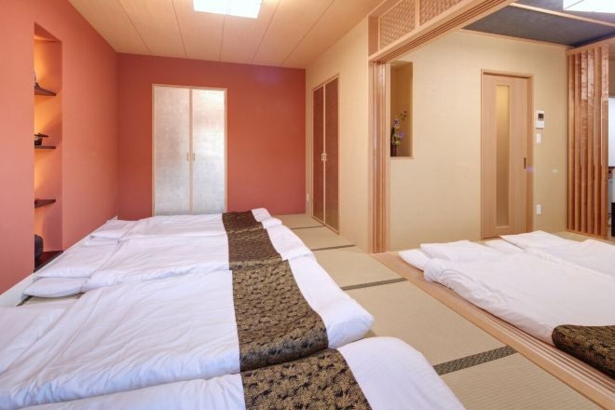 Habitación de hotel con dos camas, una puerta de madera y un estante pequeño con objetos en la pared izquierda.
