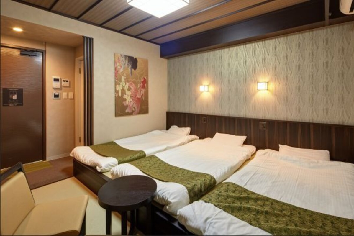 Habitación de hotel con dos camas, una mesita y una silla. Se aprecia un cuadro en la pared y un cabecero de madera.