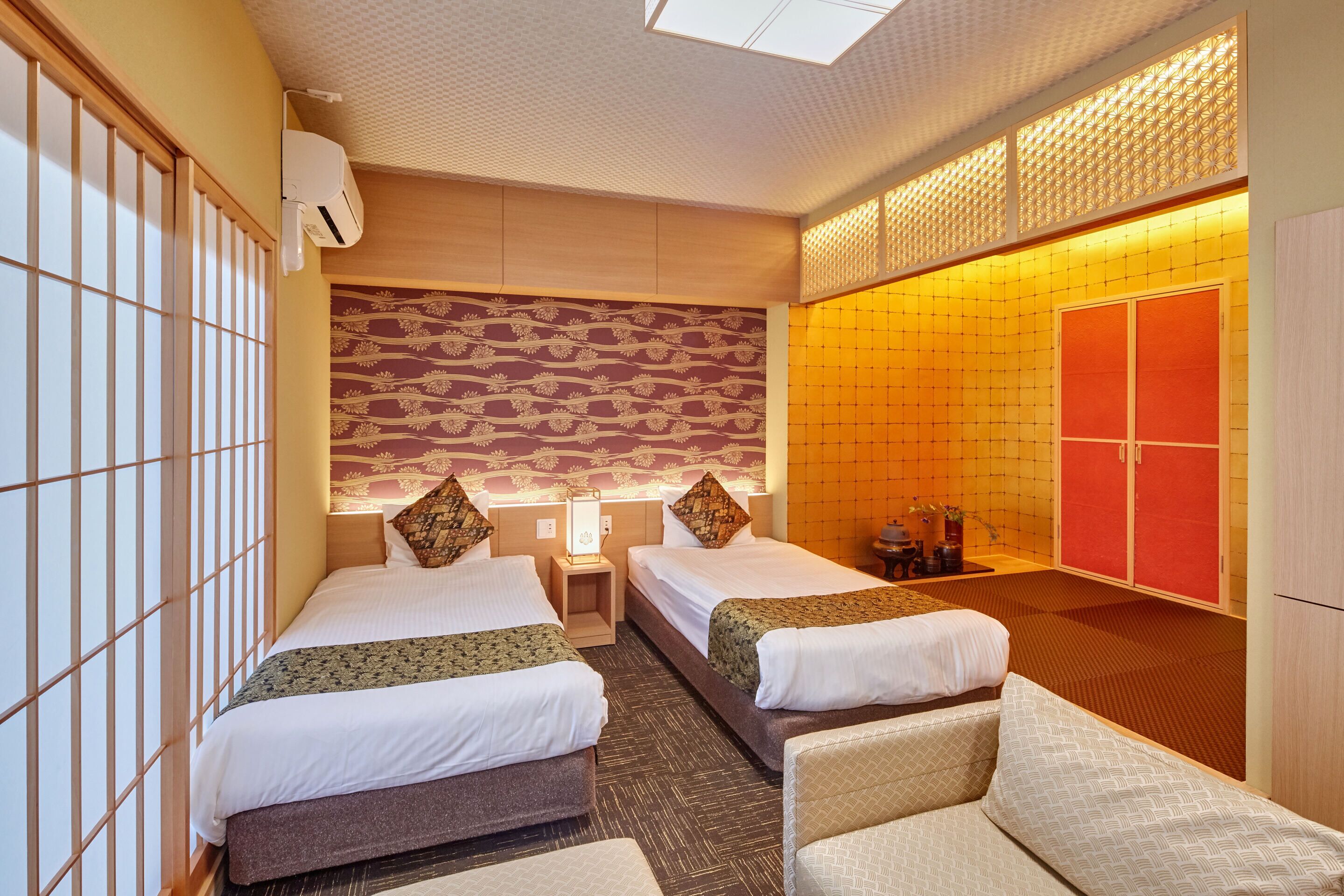 A hotel room with two beds, a sitting area, a wardrobe, and a bathroom.