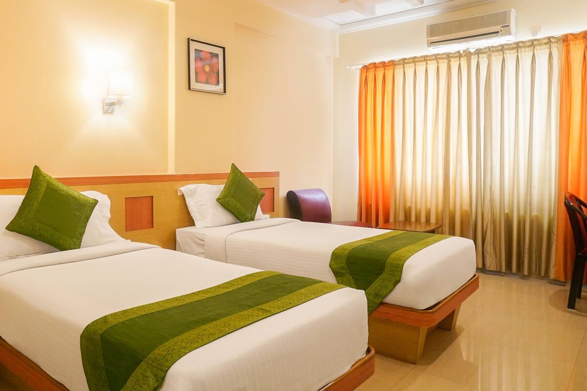 Habitación de hotel con dos camas, una silla, un cuadro en la pared y una ventana con cortinas.