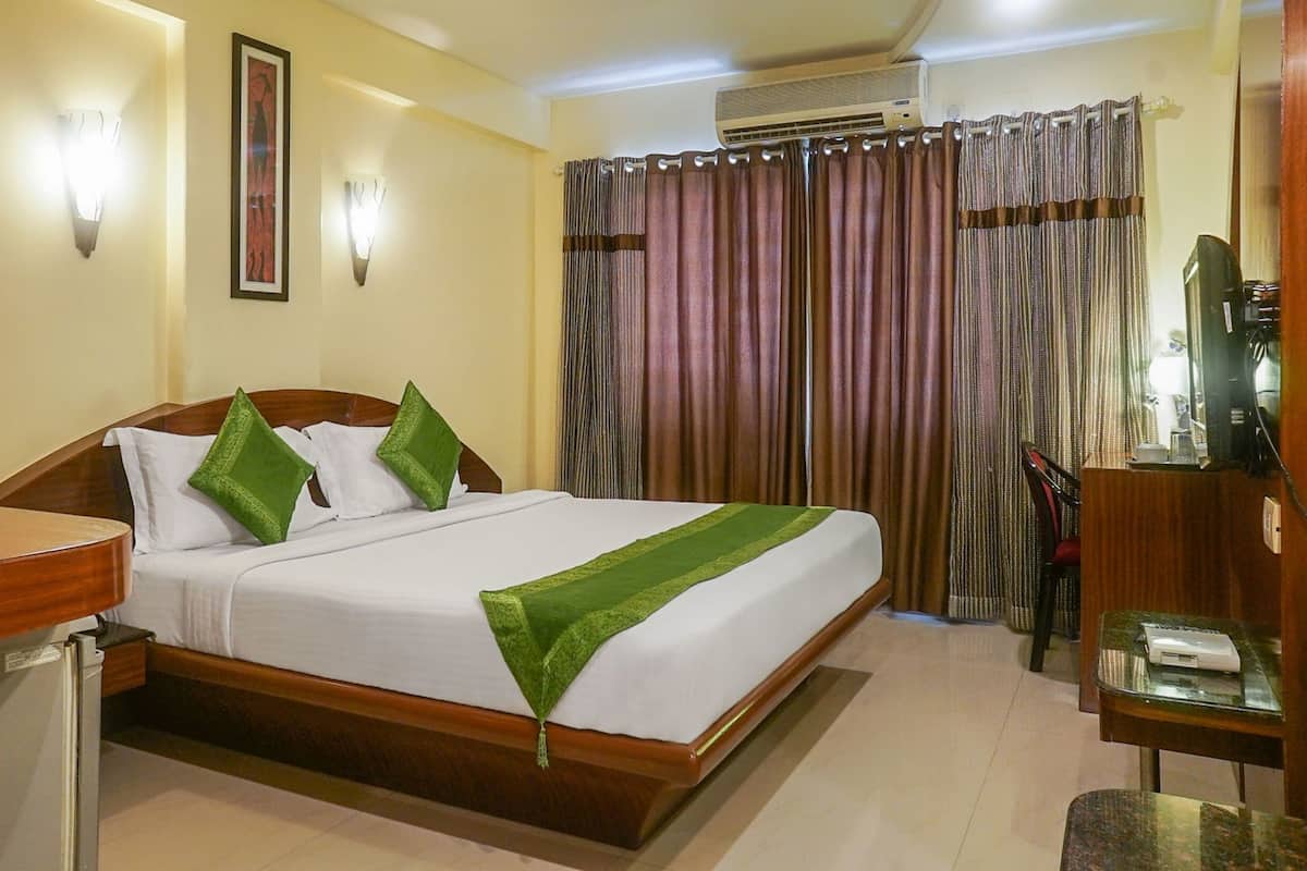 Una habitación de hotel con cama, escritorio, silla, aire acondicionado y cortinas.