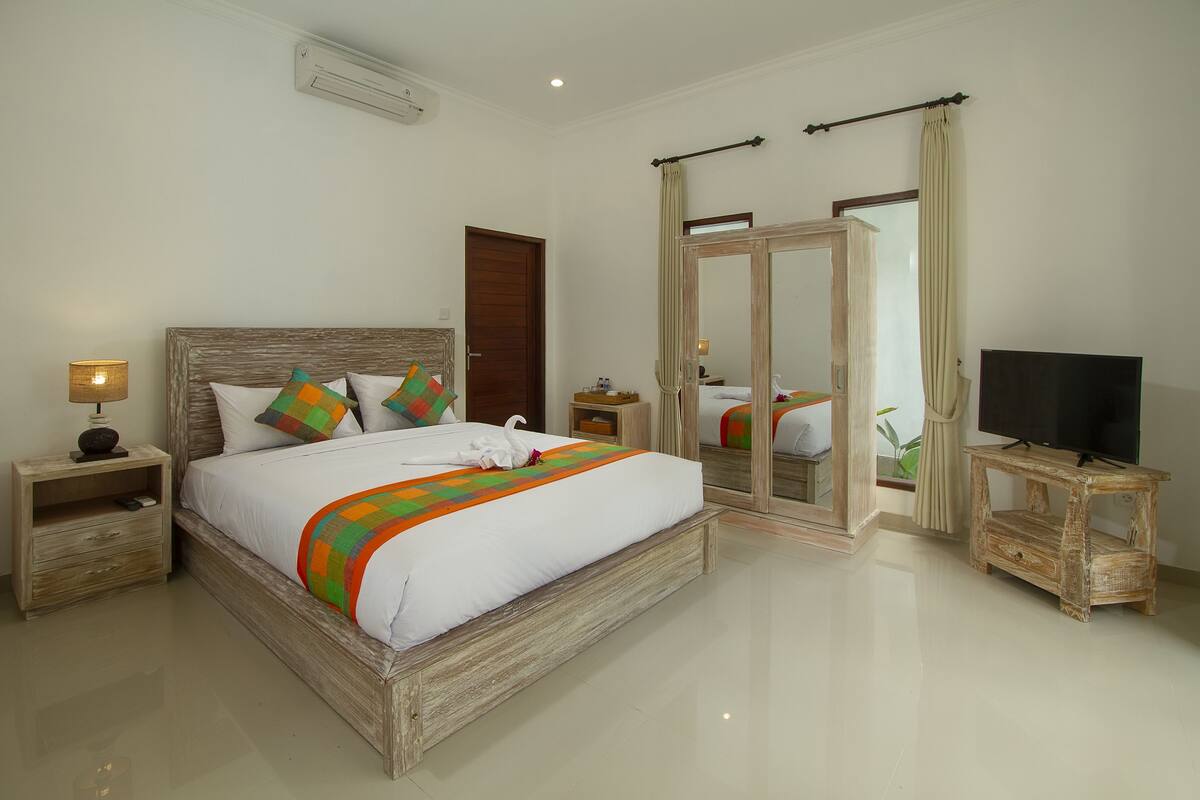 A spacious bedroom with a large bed, wooden headboard, and a television on a wooden stand.