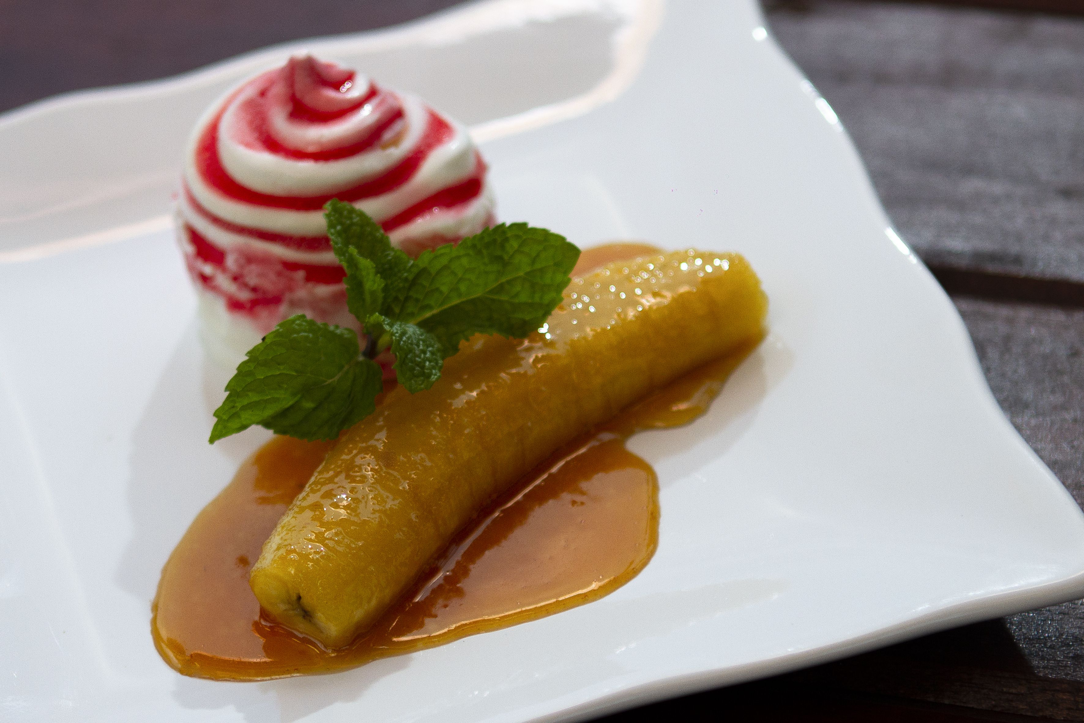 Une assiette à dessert avec une banane et un dessert aux couleurs rouge et blanc, décoré de feuilles de menthe.