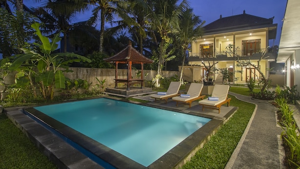 A swimming pool with lounge chairs and a gazebo, surrounded by lush greenery and palm trees, with a two-story house in the background. - Pondok Ayu Shanti (Ubud)