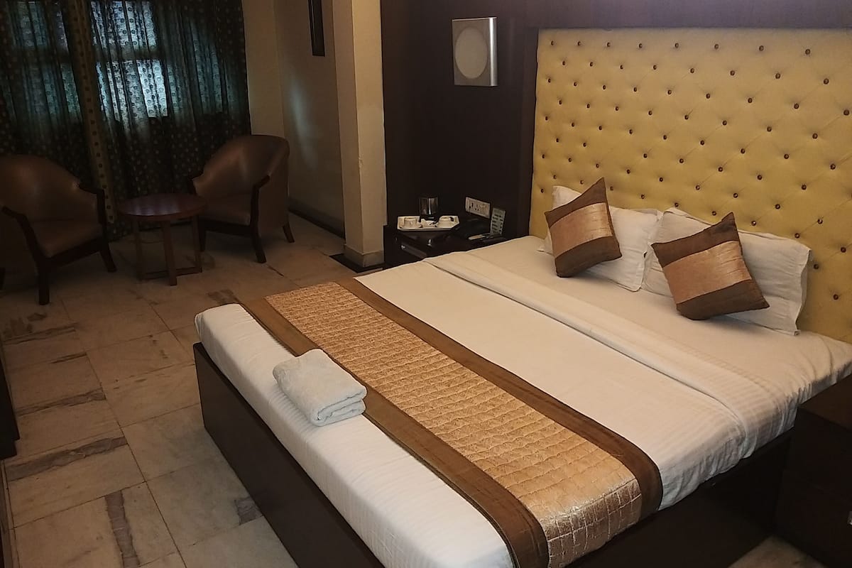 Habitación de hotel con una cama grande, dos sillas, una mesita pequeña y una mesita de noche con teléfono y taza.