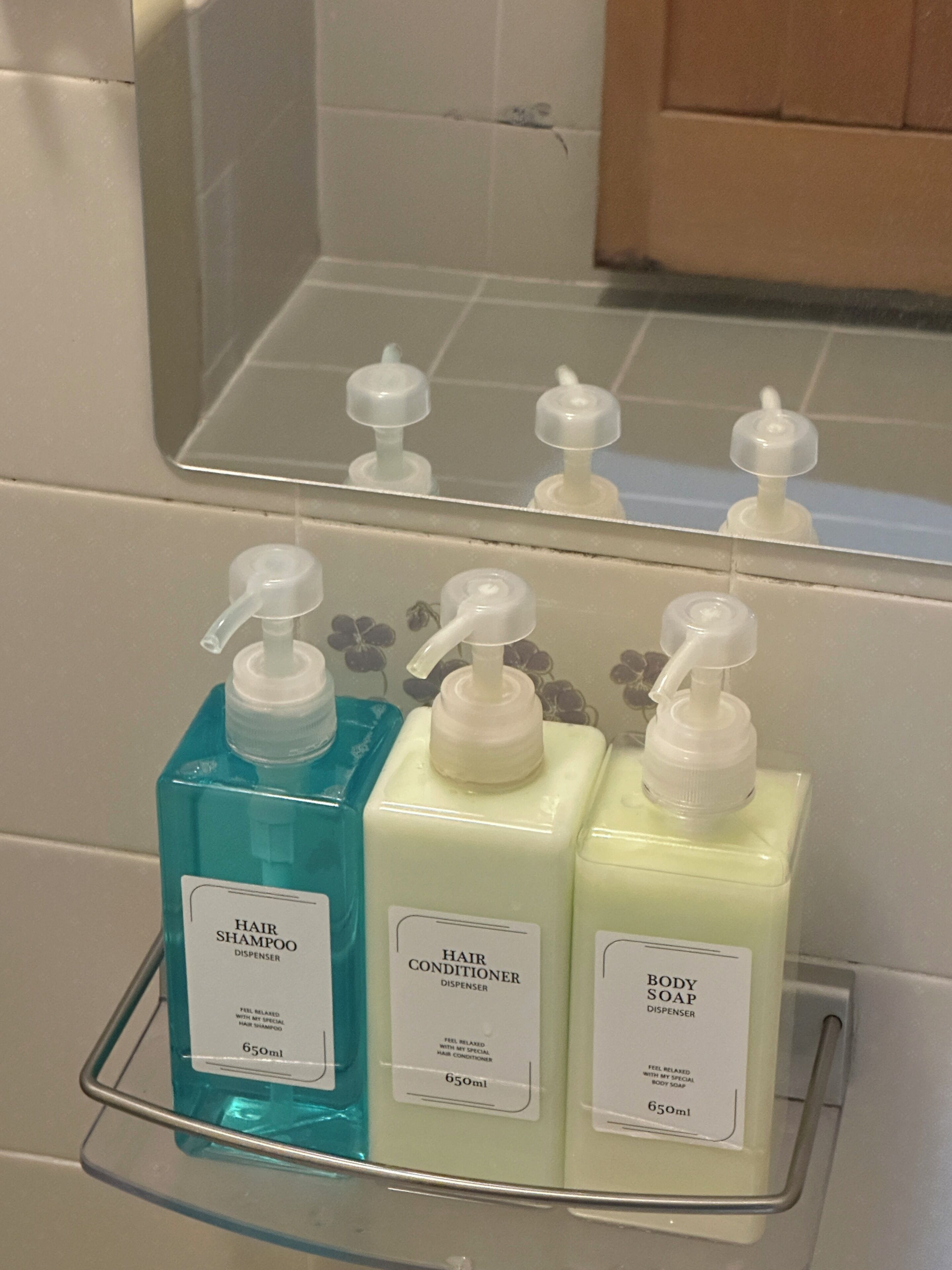 A bathroom shelf with three dispensers: hair shampoo, hair conditioner, and body soap.