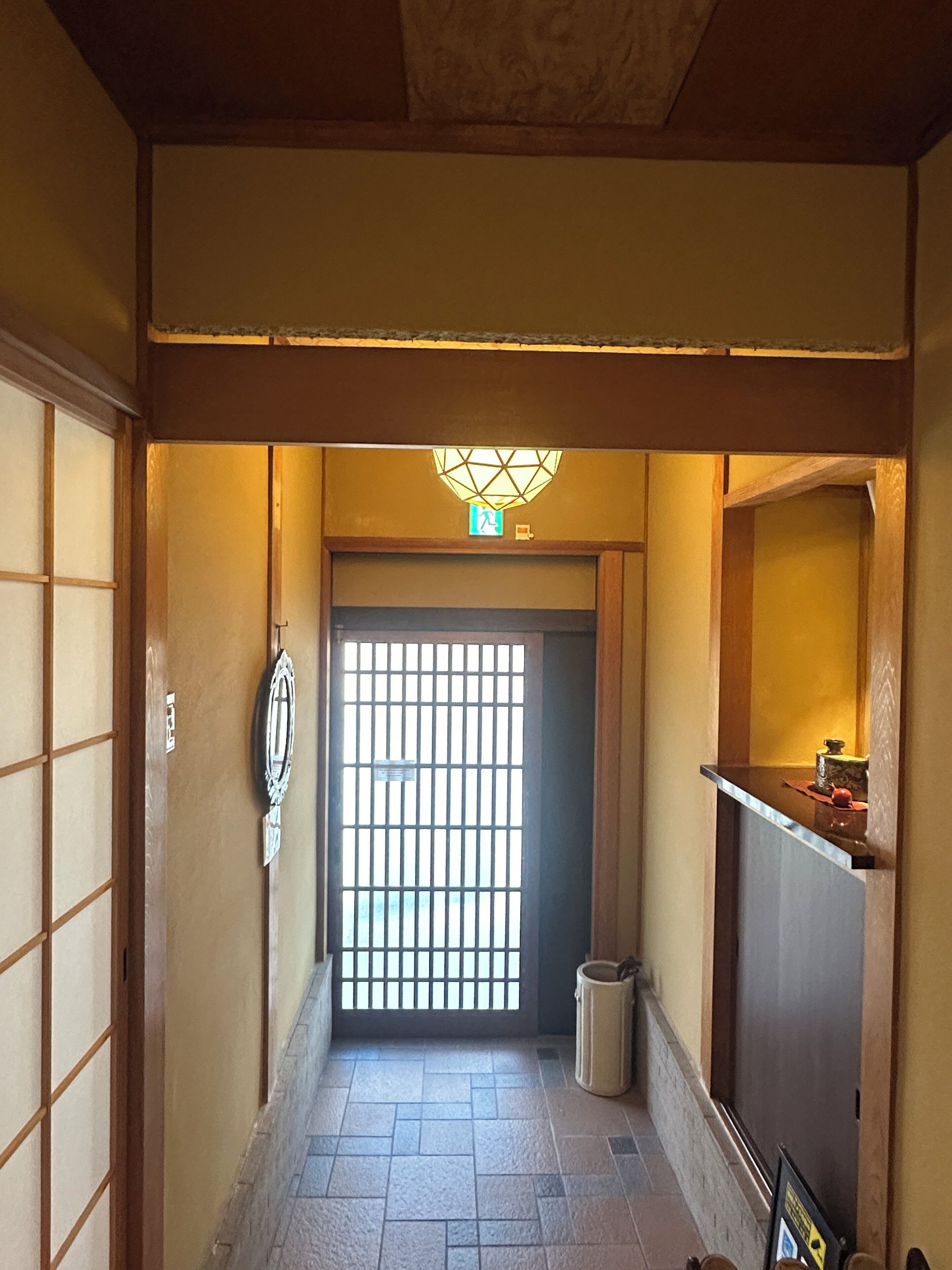A hallway with a traditional Japanese-style door, a tiled floor, and a small trash bin.