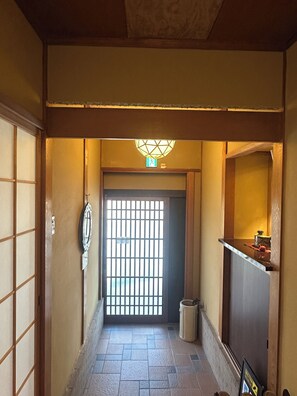 A hallway with a traditional Japanese-style door, a tiled floor, and a small trash bin. - Gallery NICO (Yao)