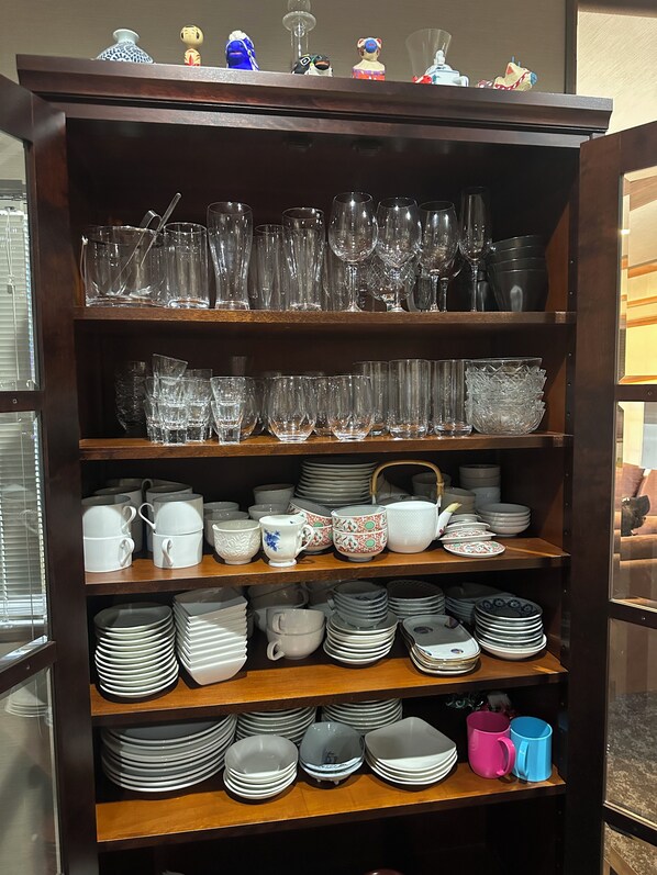 A wooden shelving unit with various glassware, cups, and plates.