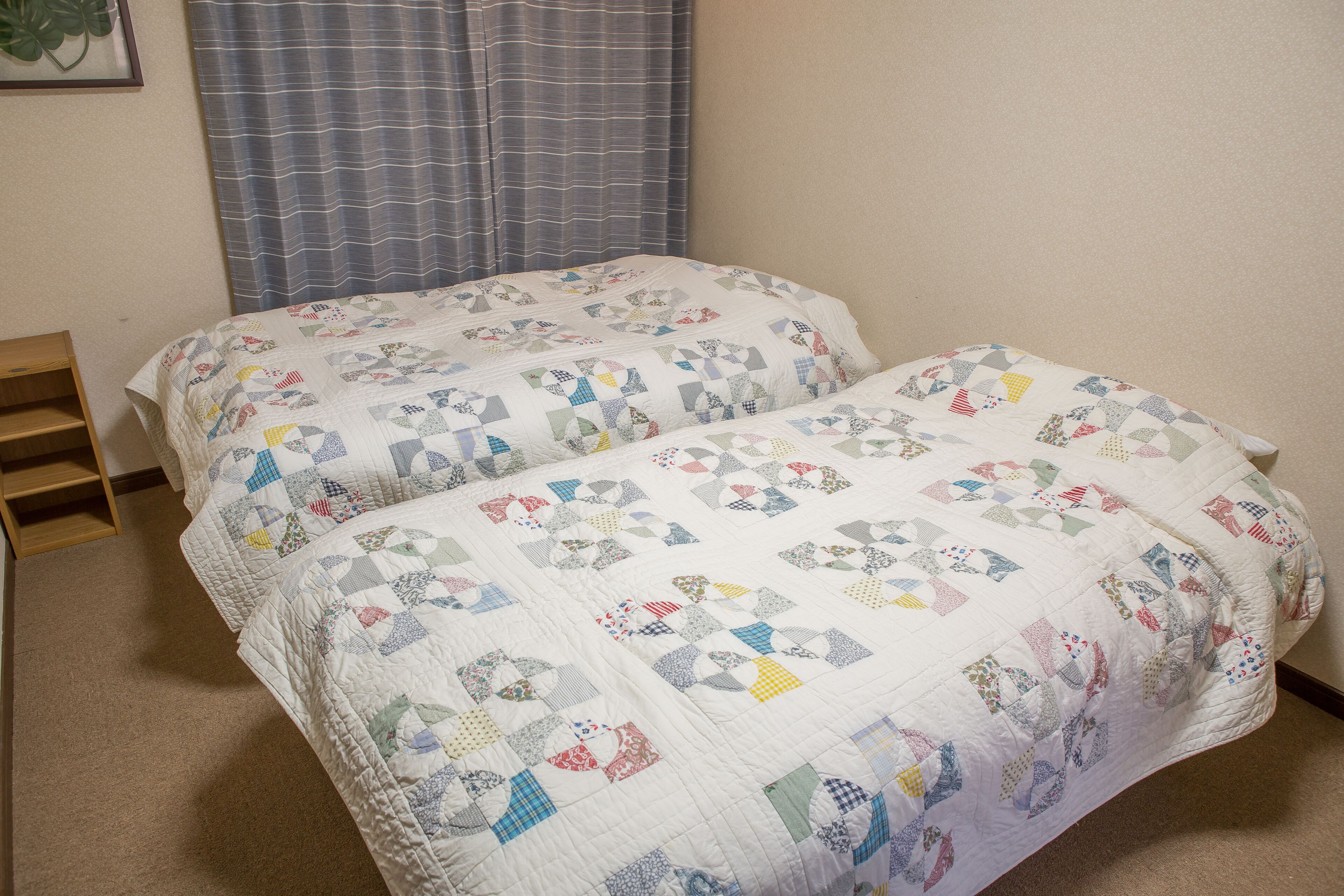 A bedroom with two beds covered in quilts, a wooden ladder, and a window with curtains.