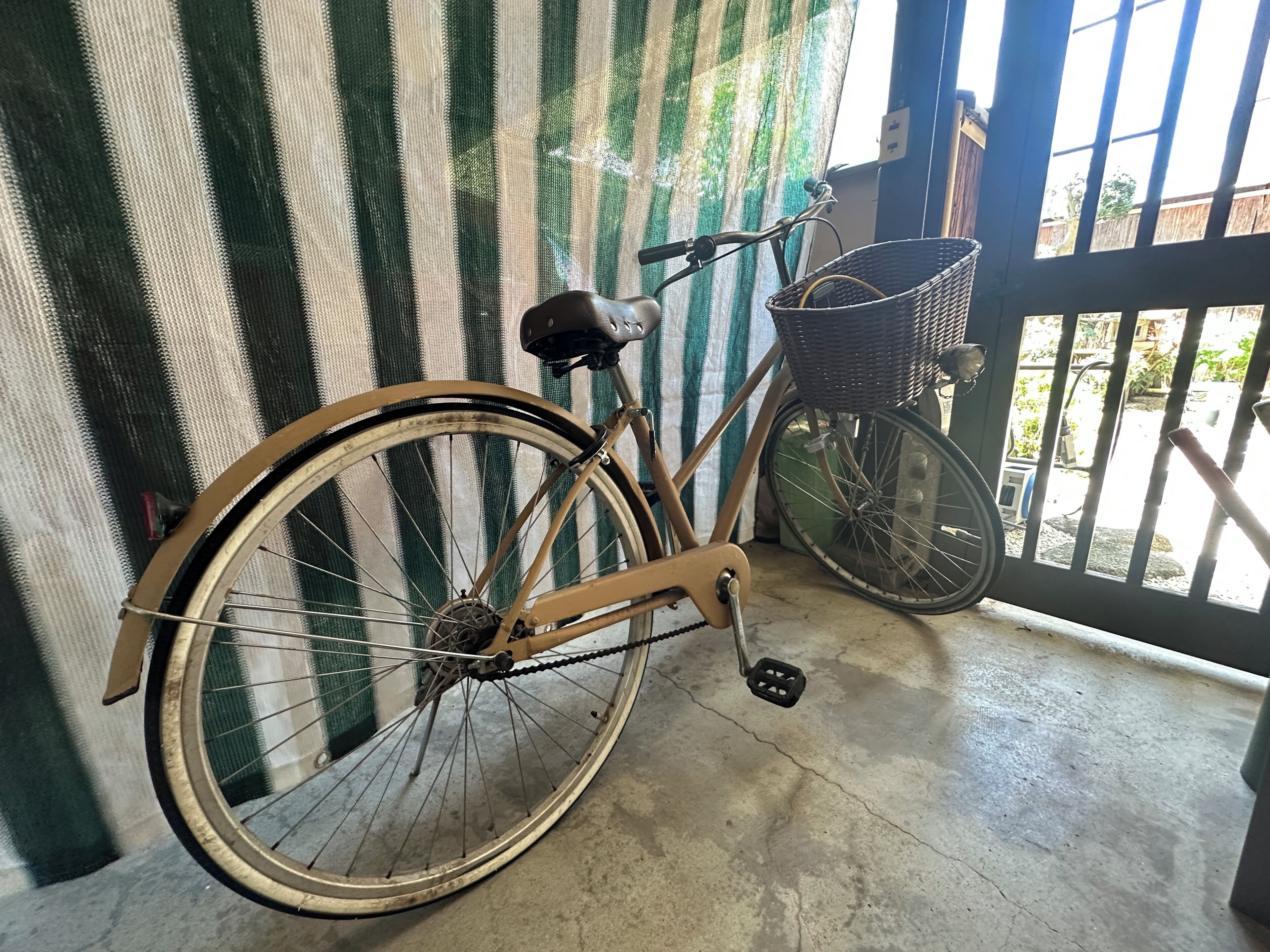 A bicycle with a basket, parked indoors with a striped curtain in the background.