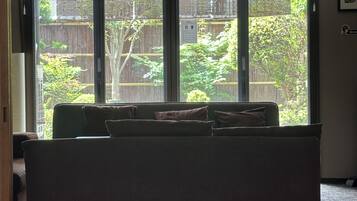 Habitación con sofá frente a un ventanal corredera que da a un balcón con vista a una cerca de madera y follaje.