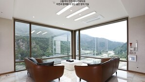 A modern room with large windows, two brown leather sofas, a white coffee table, and a view of a mountainous landscape. - Pine Forest (Jeongseon)